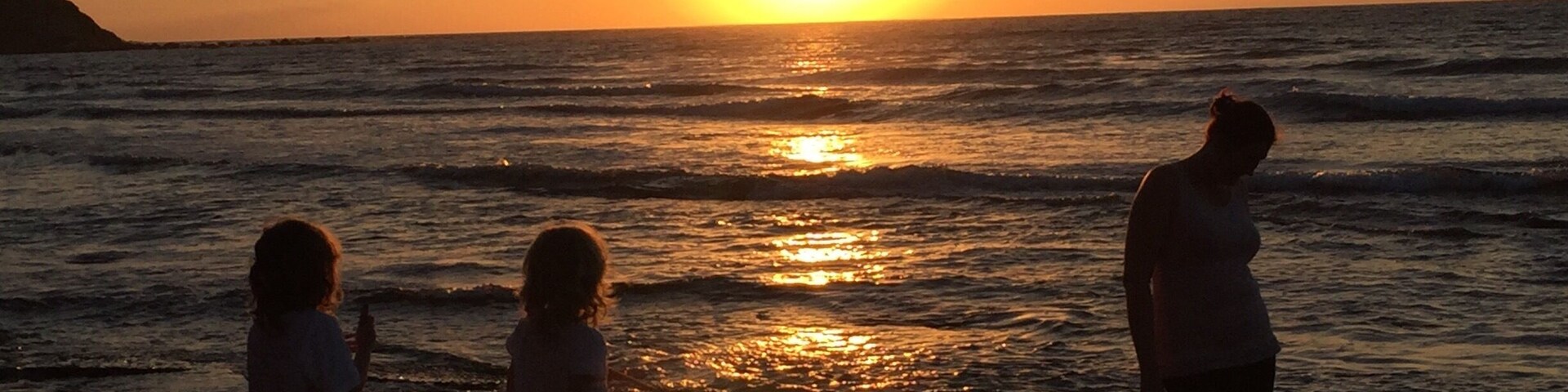 A sunset over the ocean with three people standing on the shore.