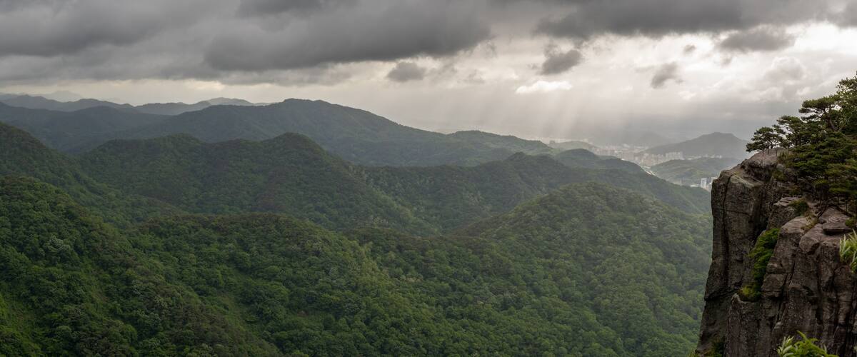 A mountainous landscape with dense green forests and a rocky cliff.