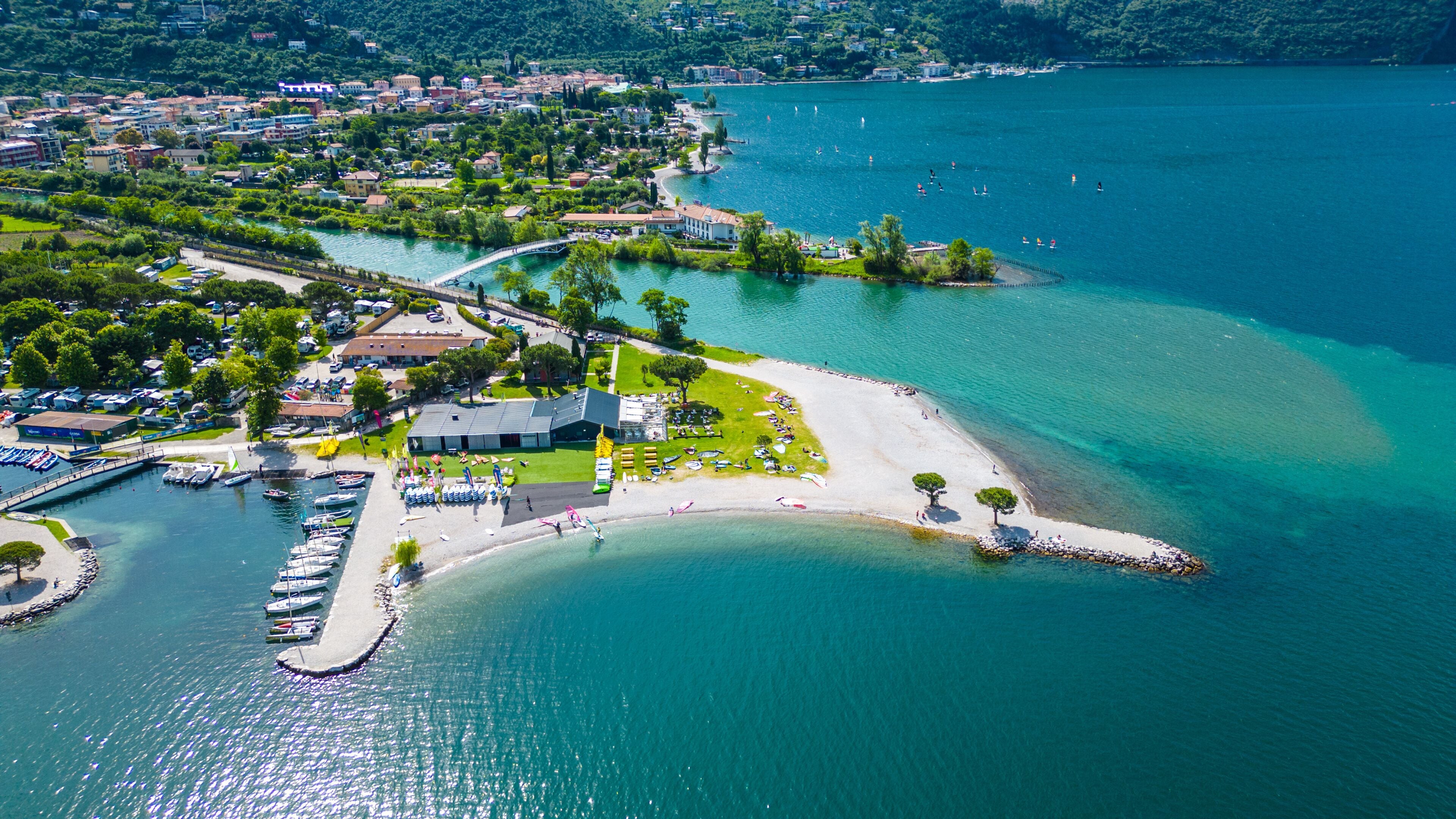 An aerial view of a coastal town with a marina, a sandy beach, and a small island with a pier.