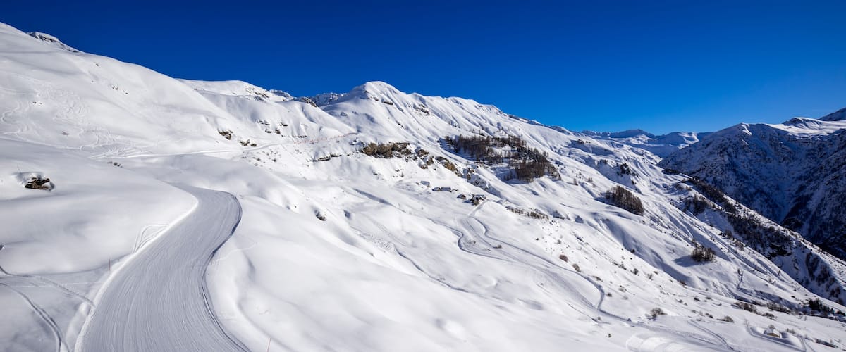 A snow-covered mountain landscape with a winding road and clear blue sky.