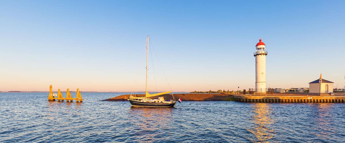 A lighthouse, a sailboat, and a breakwater.