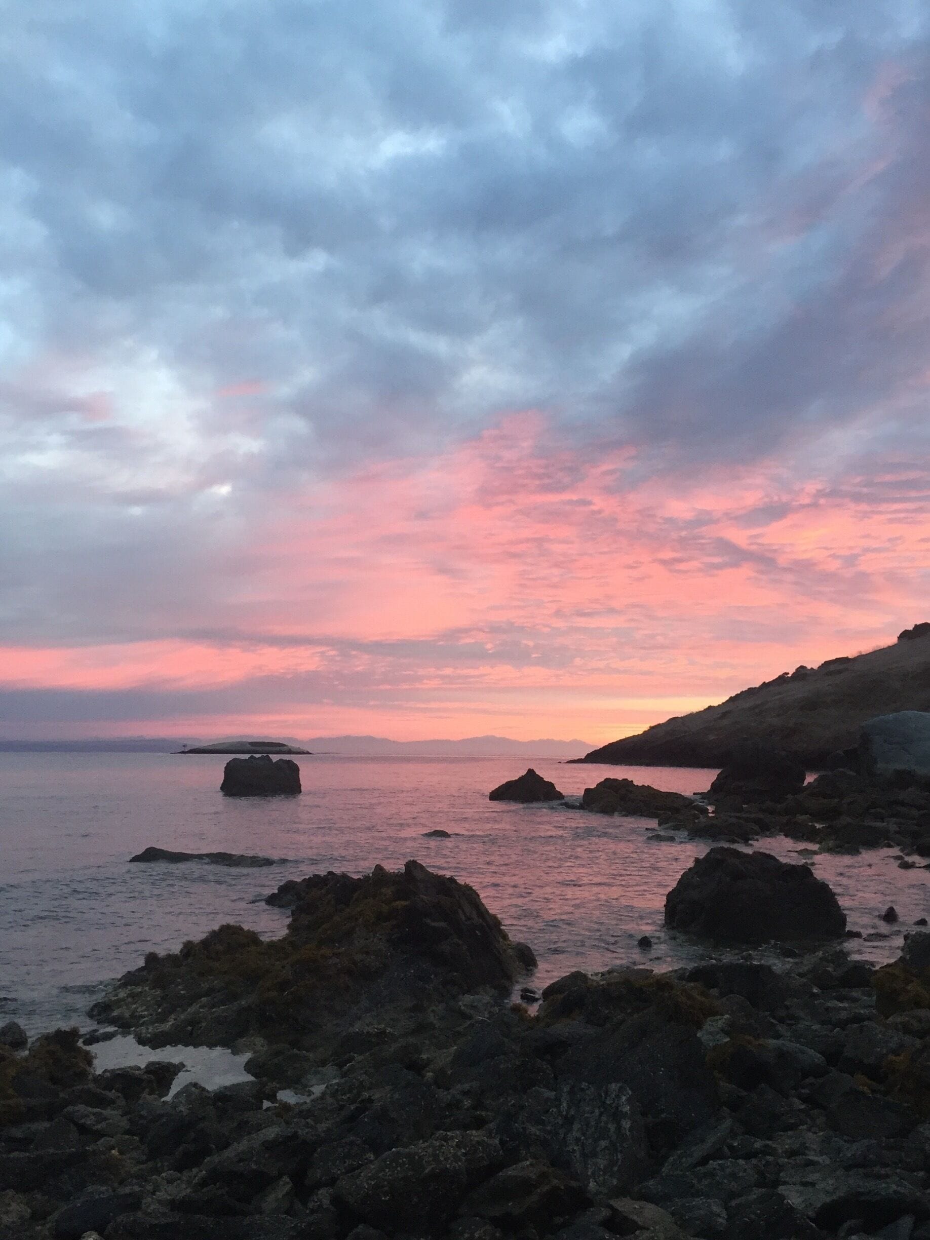 A coastal landscape with rocky outcrops and a sunset sky.