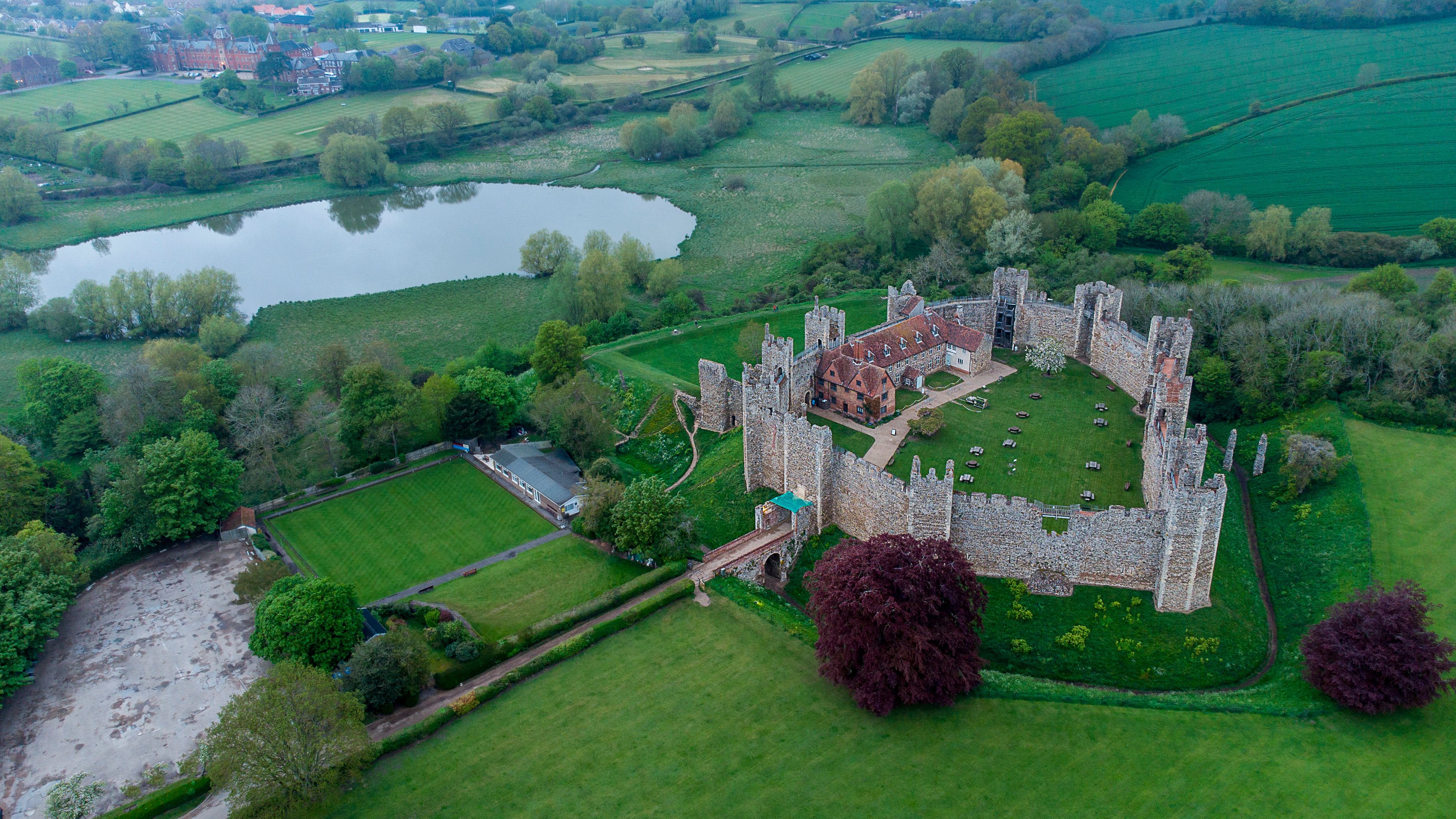 An aerial view of a historic castle surrounded by lush green fields and a body of water.