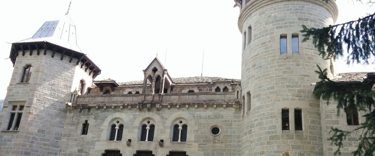 A historic stone building with arched windows, a turret, and a bell tower.