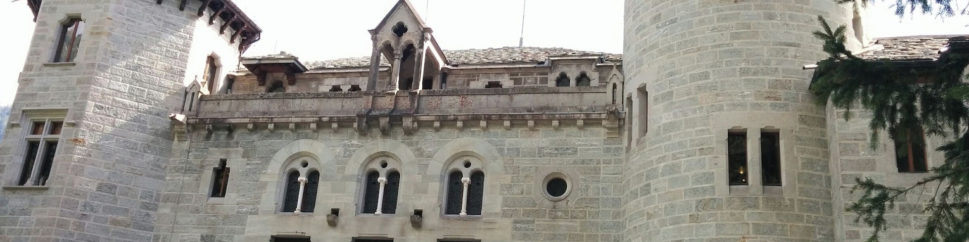A historic stone building with arched windows, a turret, and a bell tower.