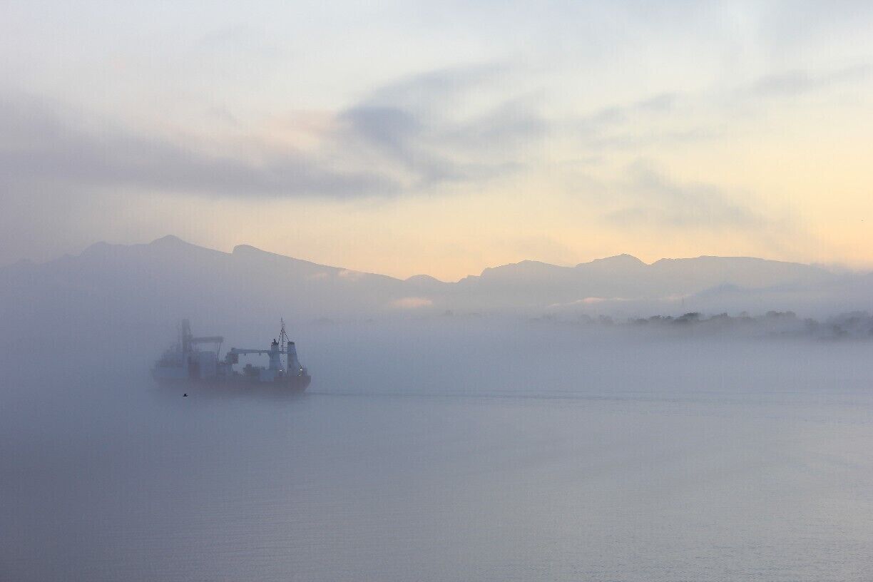 A foggy landscape with mountains in the background and a ship in the foreground.