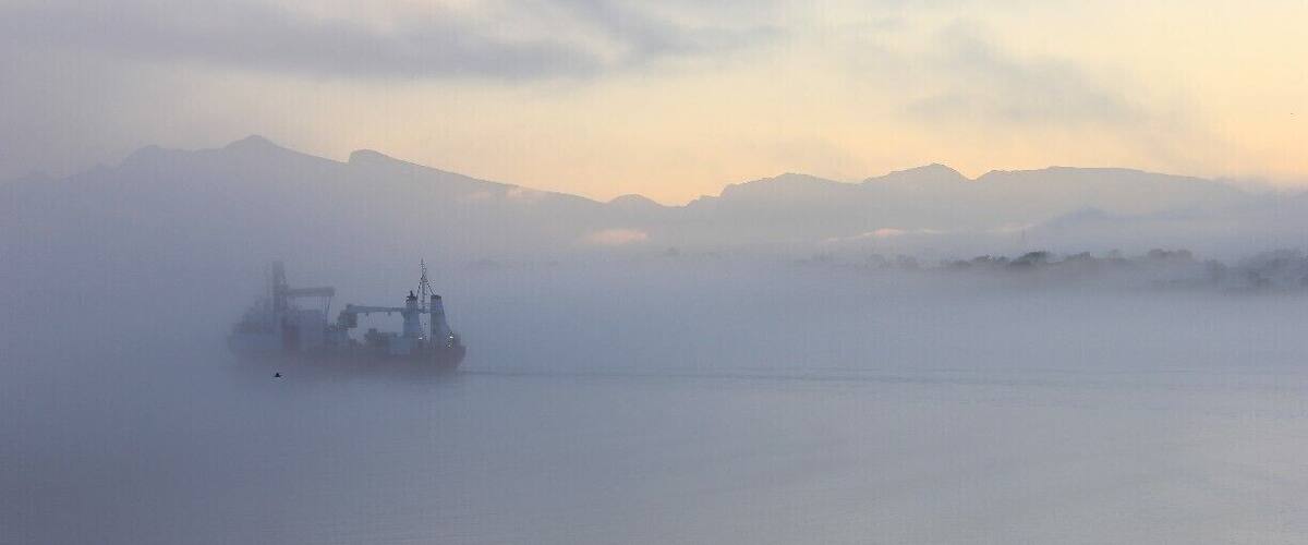 A foggy landscape with mountains in the background and a ship in the foreground.