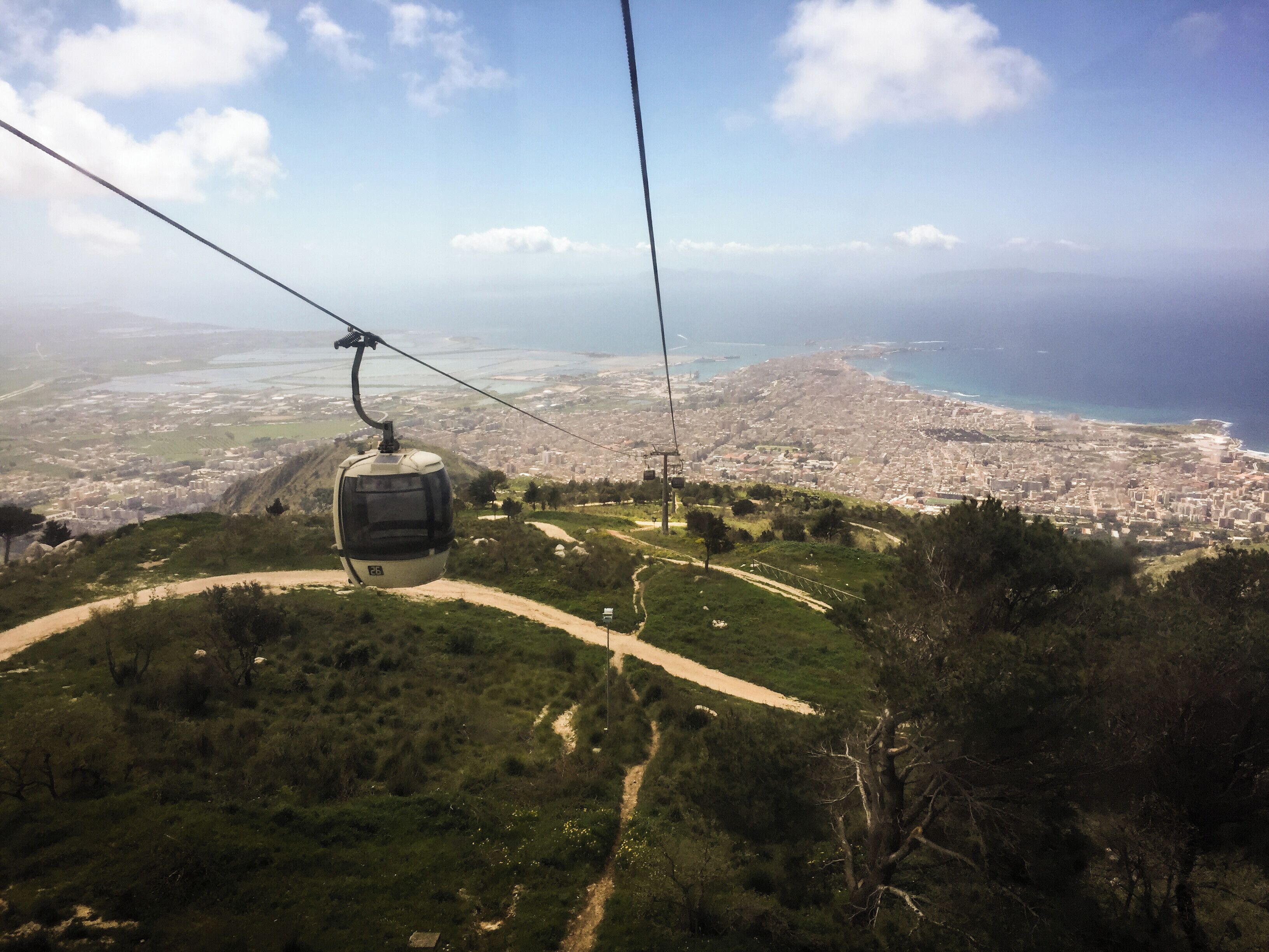A cable car over a coastal city with a clear view of the sea and urban landscape.