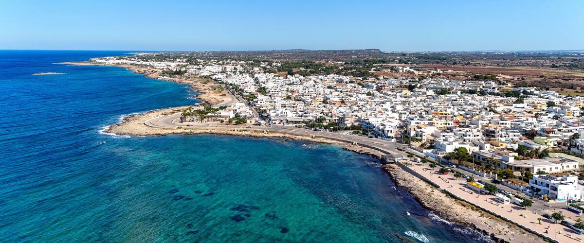 A coastal town with a clear blue sea, white buildings, and a rocky shoreline.