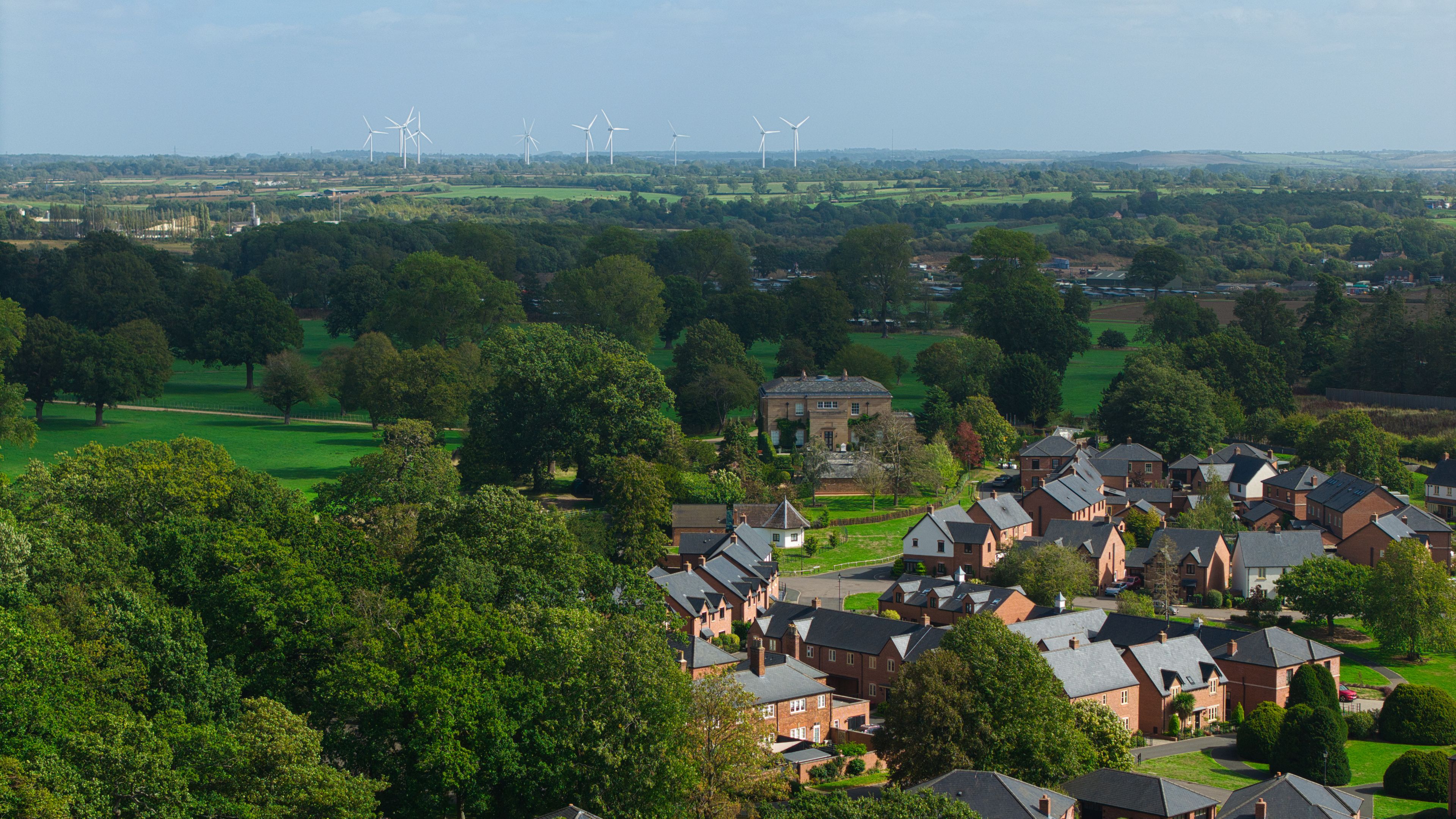Un quartier résidentiel avec des maisons, des champs verdoyants et, au loin, des éoliennes.