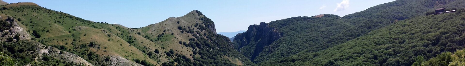 Paisaje montañoso con un pico rocoso destacado y valles verdes exuberantes.