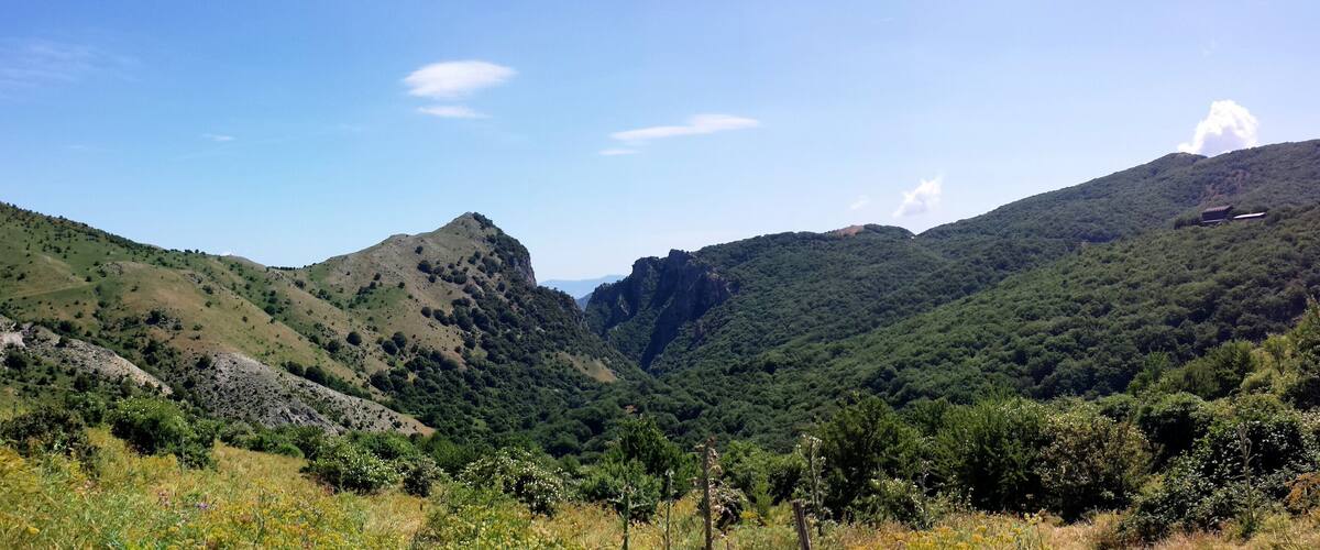 A mountainous landscape with green hills, a valley, and a small building on a hill.