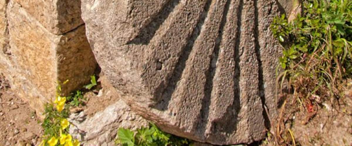A stone sundial with a circular design and radiating lines, set against a stone wall.