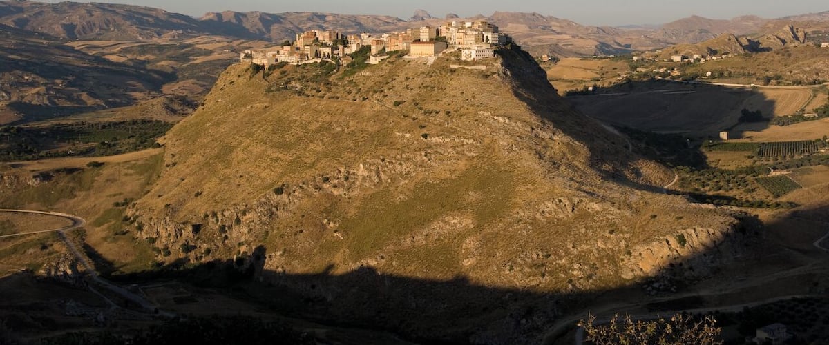 A historic fortified town on a hill with surrounding mountainous terrain.