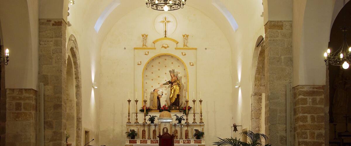 An interior of a church with wooden pews, a central altar, and a chandelier.