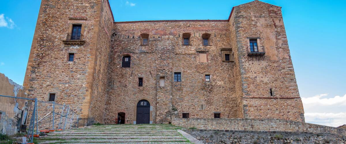 A historic stone castle with a central tower, arched windows, and a large entrance.