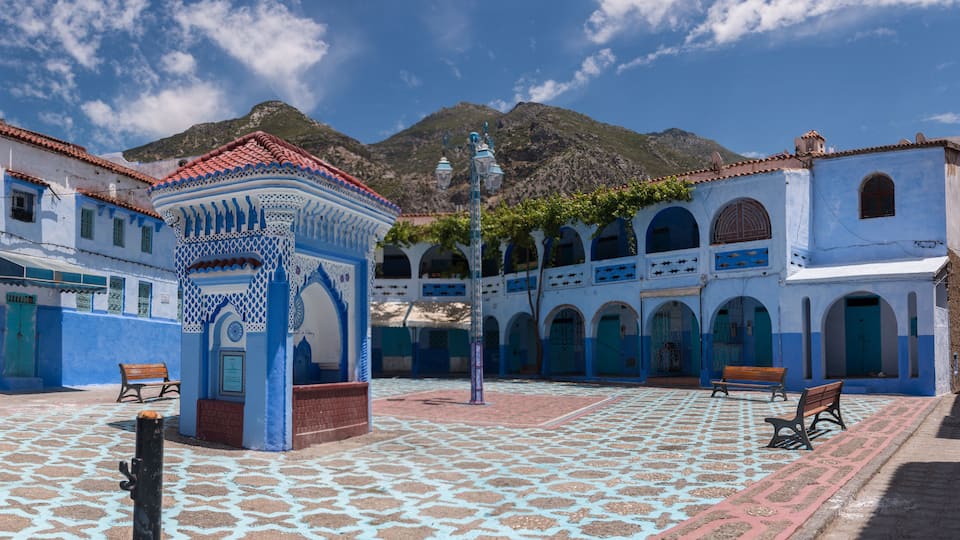 A courtyard with patterned tiles, benches, and a gazebo with blue and white walls.