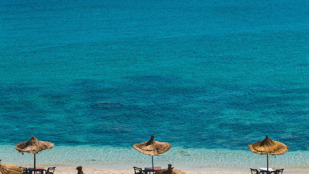 A beach with clear turquoise water, straw umbrellas, and tables set up for dining.
