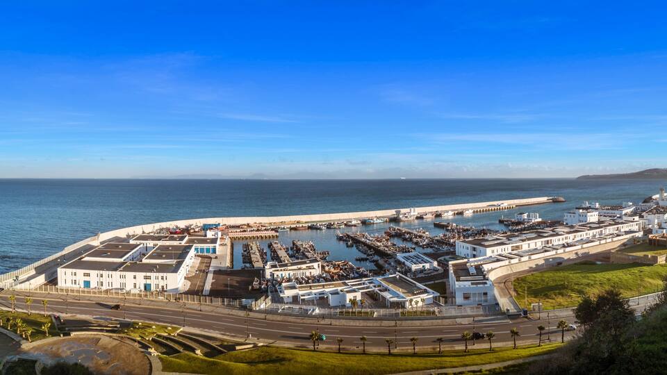 A coastal cityscape with a marina, white buildings, and a clear blue sky.