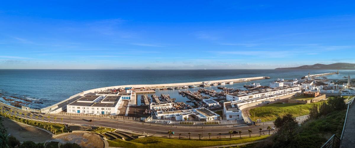 A coastal cityscape with a marina, white buildings, and a clear blue sky.