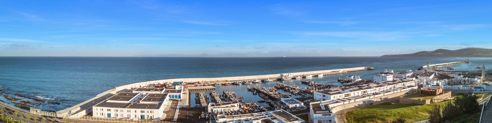 A coastal cityscape with a marina, white buildings, and a clear blue sky.