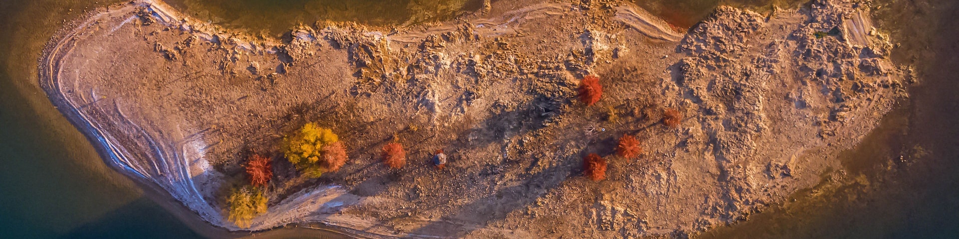 An aerial view of a coastal area with a curved shoreline, rocky terrain, and sparse vegetation.
