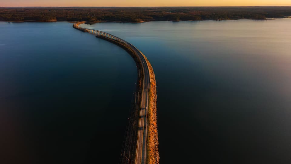 A long bridge curving through a calm body of water, surrounded by forested land.
