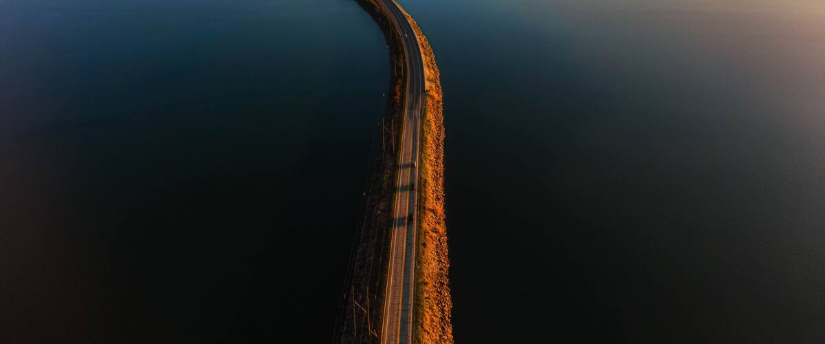 A long bridge curving through a calm body of water, surrounded by forested land.