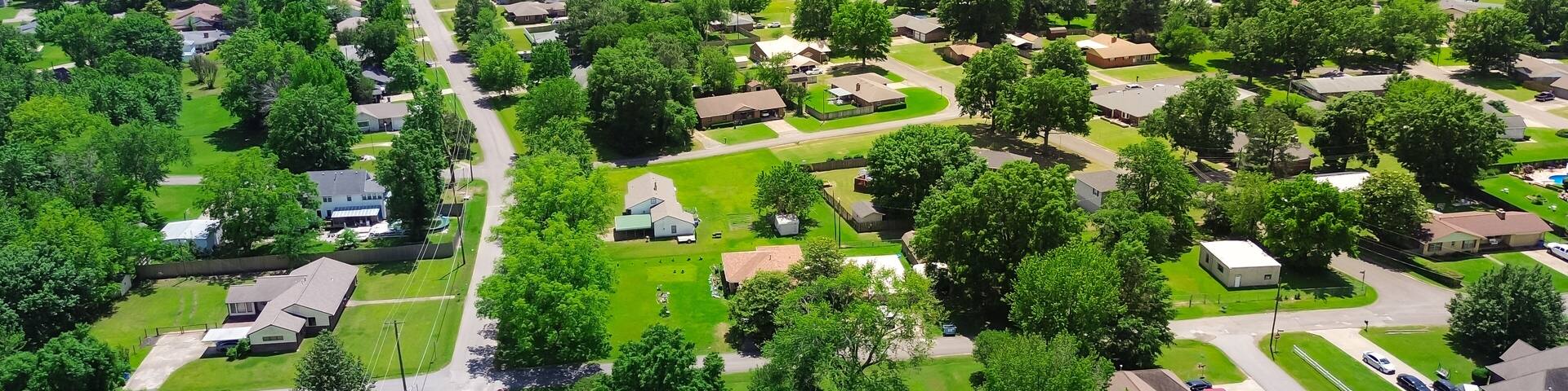 SW 4th street in Checotah, McIntosh County, Oklahoma with Interstate I-40 and water tower in background, row of single-family homes with large backyard, surrounding by lush green trees, aerial