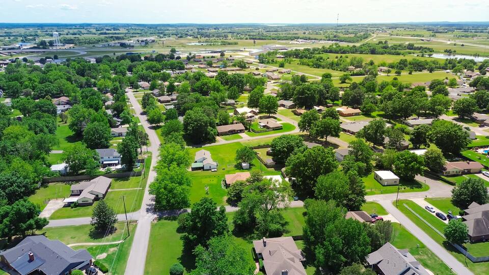 SW 4th street in Checotah, McIntosh County, Oklahoma with Interstate I-40 and water tower in background, row of single-family homes with large backyard, surrounding by lush green trees, aerial