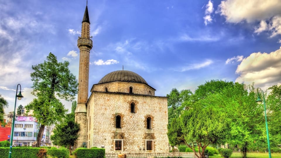 Un bâtiment historique doté d’un haut minaret et d’un dôme, entouré d’arbres et surplombant un ciel dégagé.
