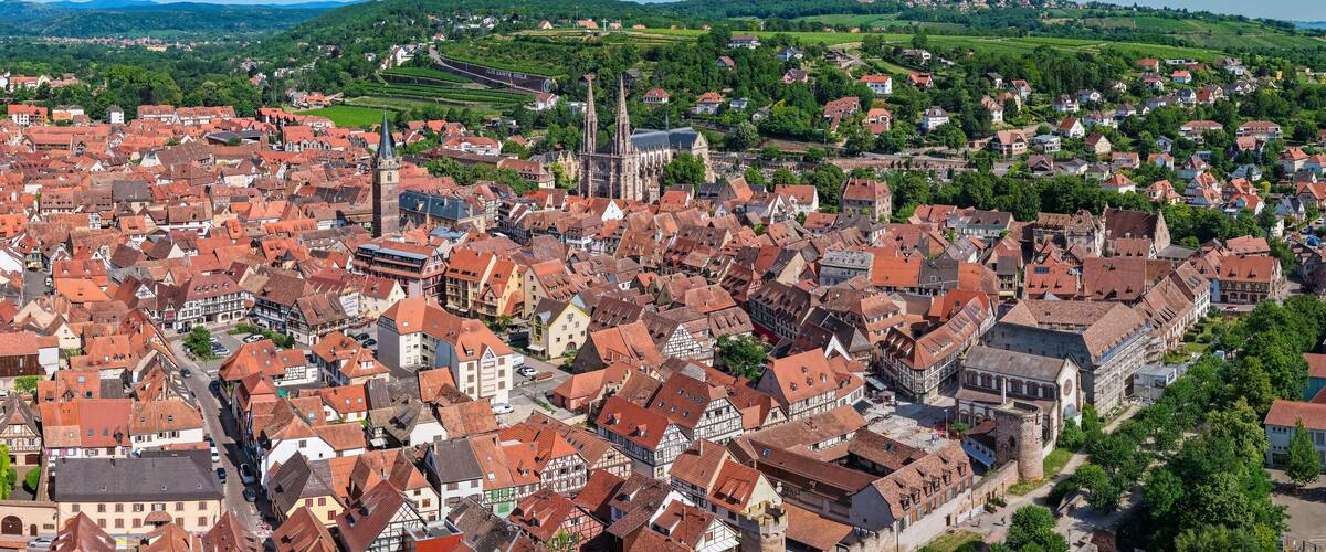 A historic town with red-roofed buildings, a prominent church, and rolling hills in the background.
