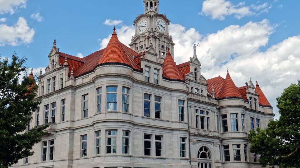 A large, historic building with a clock tower and red-tiled roofs.
