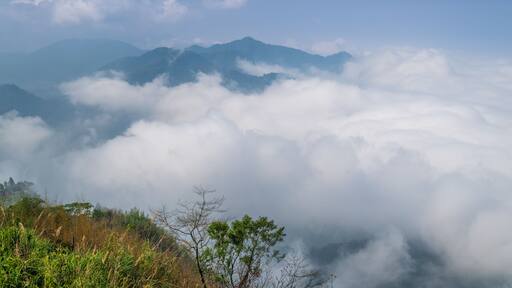 A serene view of the mist-covered mountains in Fanlu Township, Chiayi County, Taiwan, captured on a spring afternoon. The dense fog creates a mystical atmosphere, enveloping the lush green hills.