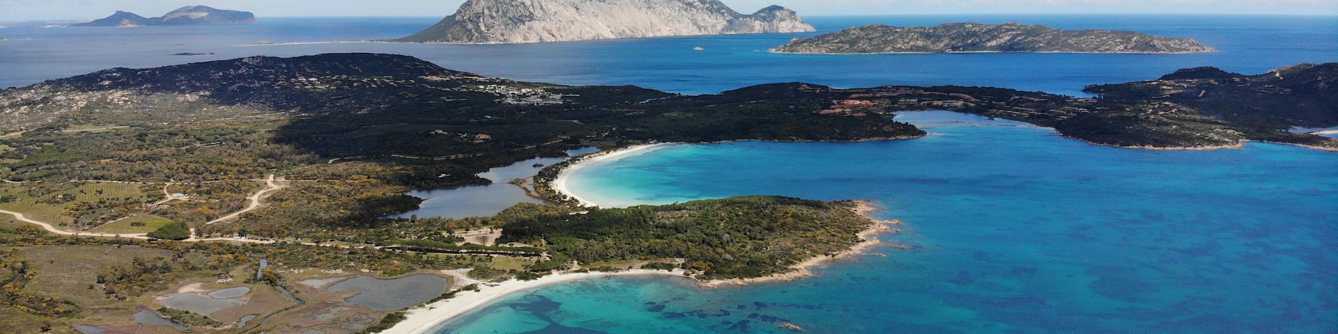 A coastal landscape with a prominent mountain, clear turquoise waters, and a sandy beach.