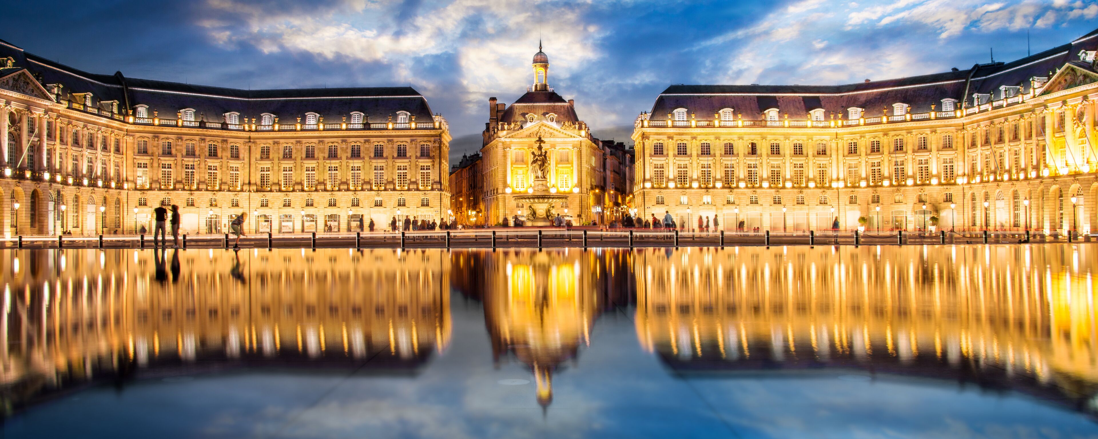 A grand palace with a symmetrical facade, a central dome, and a reflection in the water.
