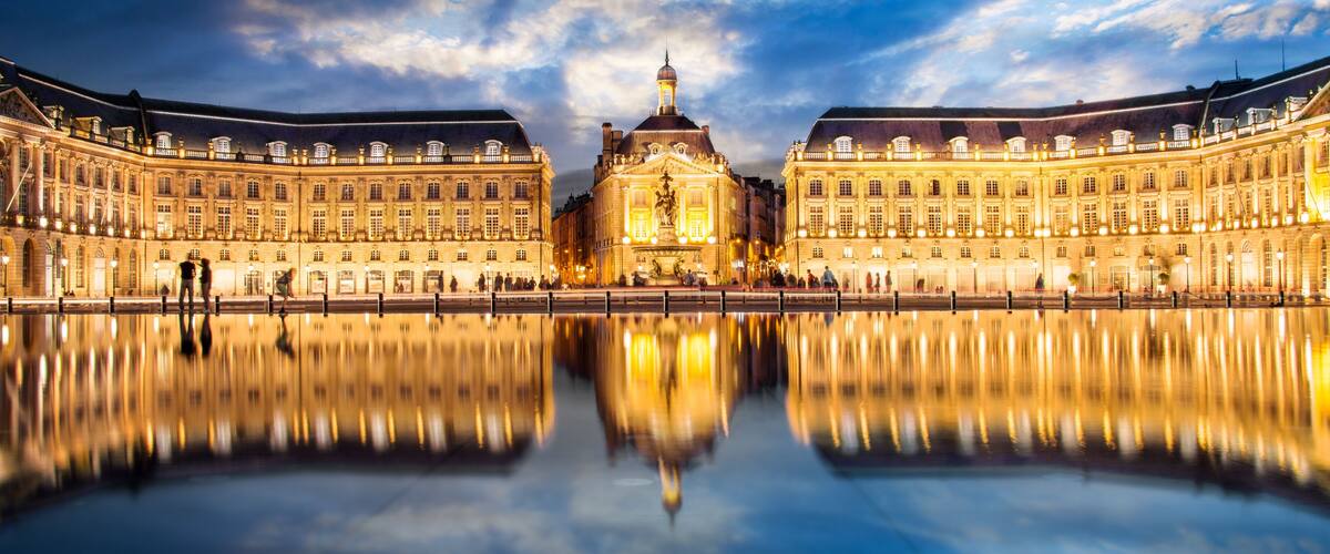 A grand palace with a symmetrical facade, a central dome, and a reflection in the water.