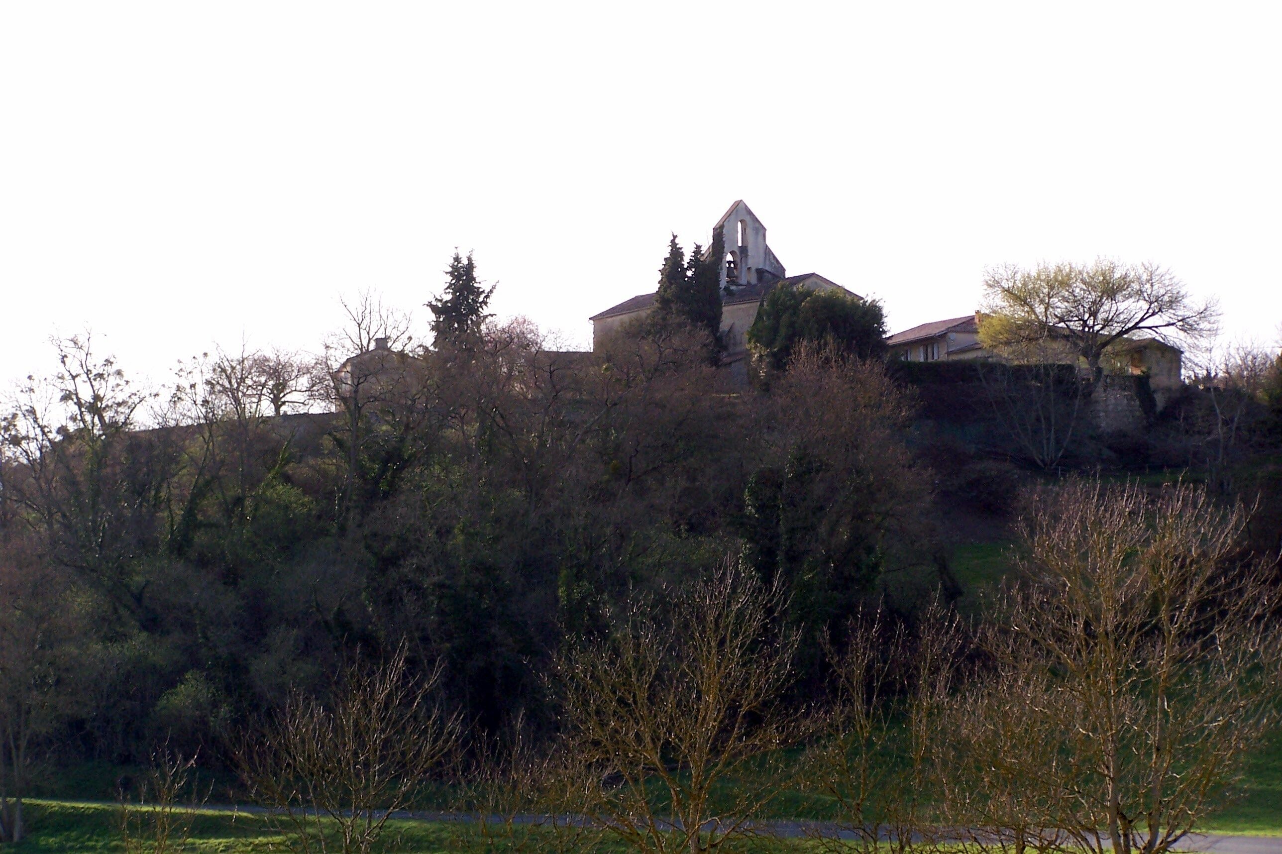 A church with a bell tower on a hill, surrounded by trees and a small building.