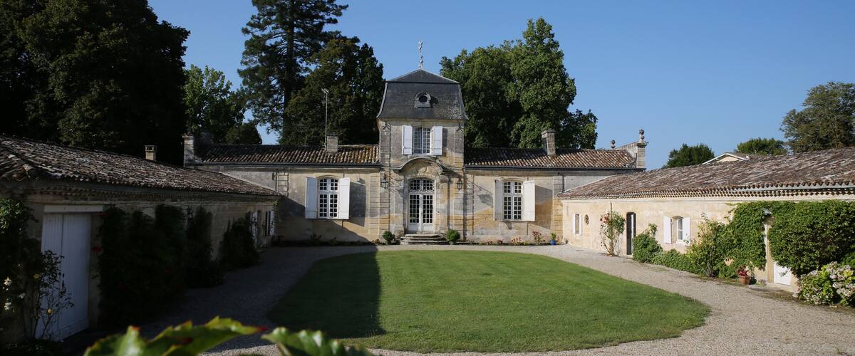 A historic building with a central tower, surrounded by a well-maintained garden and trees.