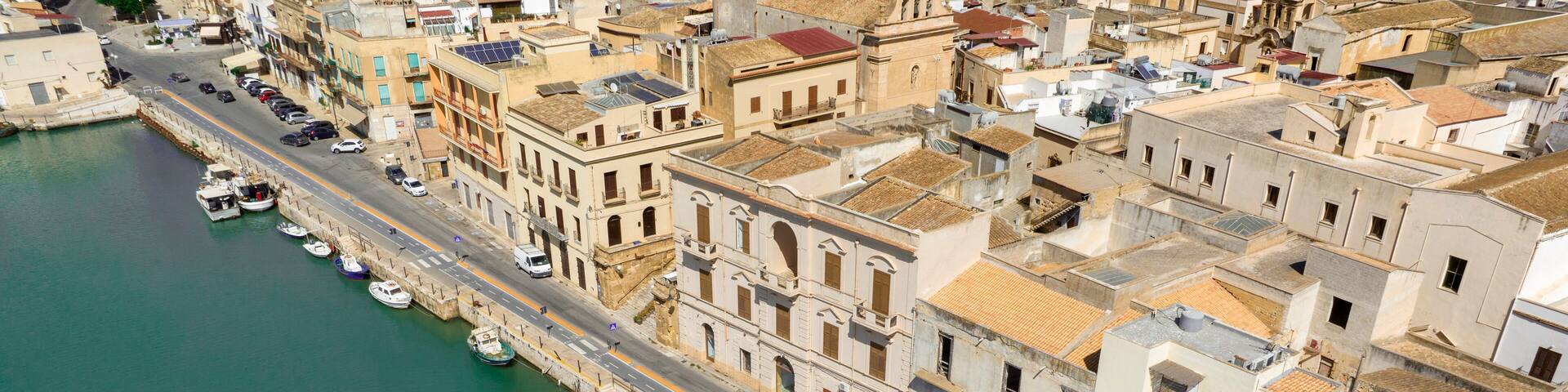 Aerial view of houses and buildings built along a canal. It's Mazaro river, located in the historic center of Mazara del Vallo, in the province of Trapani, Sicily, Italy. It's a beautiful sunny day.
