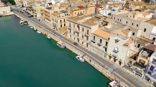 Aerial view of houses and buildings built along a canal. It's Mazaro river, located in the historic center of Mazara del Vallo, in the province of Trapani, Sicily, Italy. It's a beautiful sunny day.