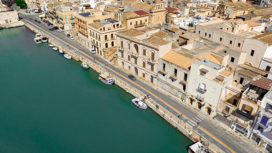 Aerial view of houses and buildings built along a canal. It's Mazaro river, located in the historic center of Mazara del Vallo, in the province of Trapani, Sicily, Italy. It's a beautiful sunny day.