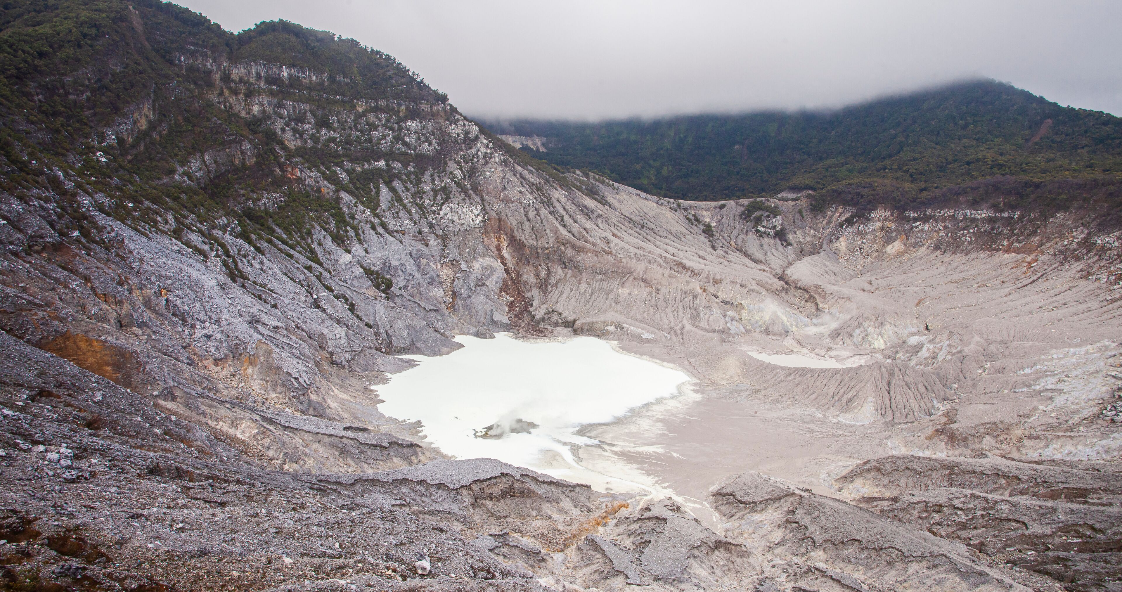 A large crater with a small lake surrounded by rocky terrain and forested hills.