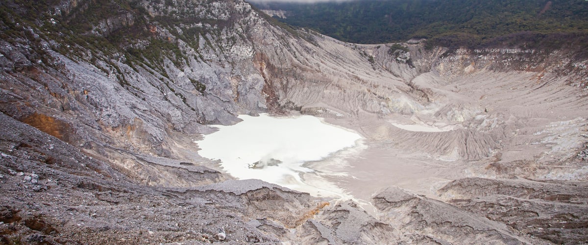 A large crater with a small lake surrounded by rocky terrain and forested hills.
