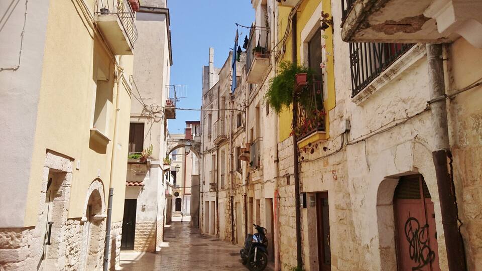 A narrow street lined with old buildings, some with balconies and laundry hanging out to dry.