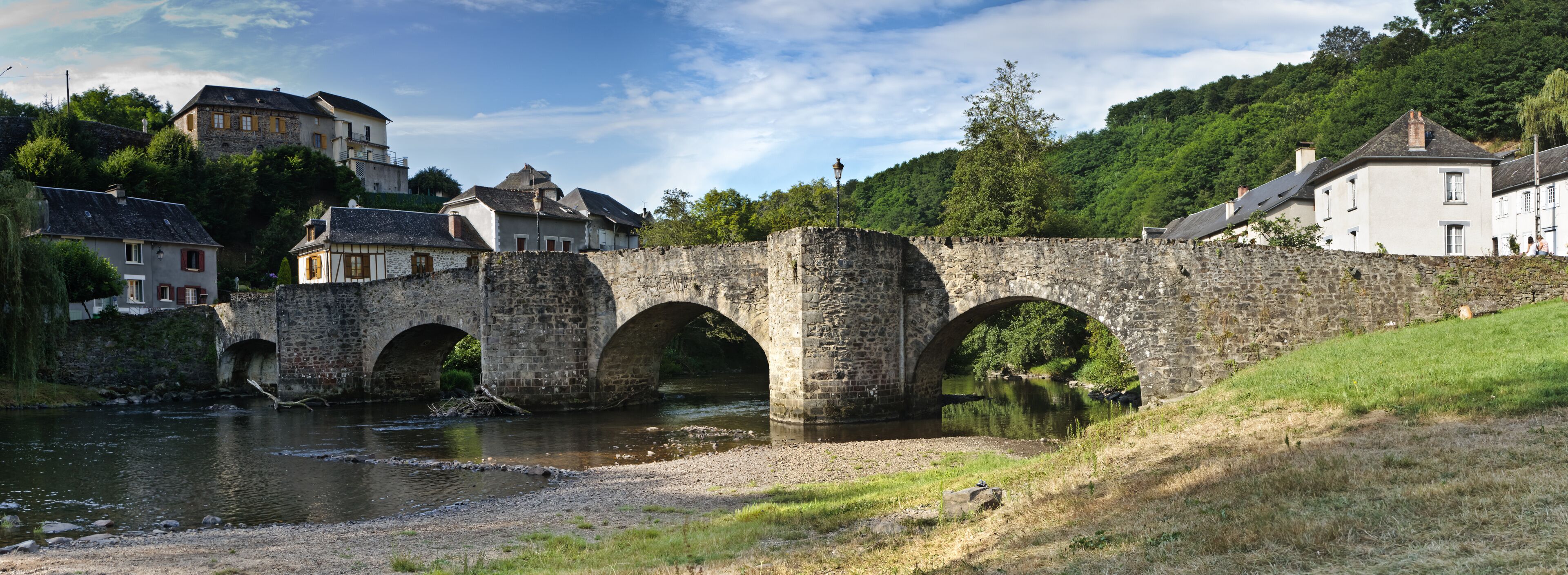 A stone bridge over a river with houses on the hillside.