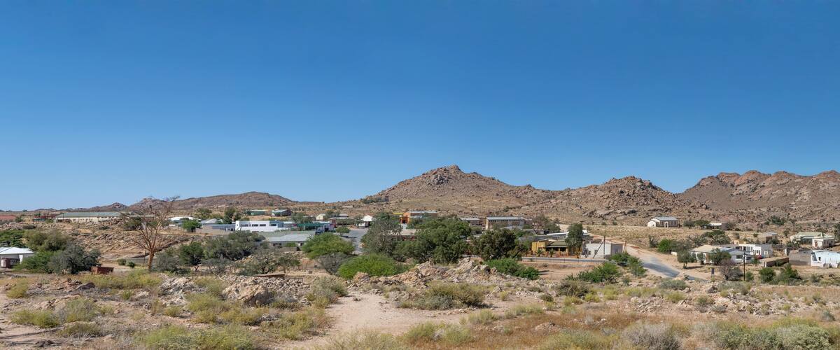 A desert landscape with scattered buildings, rocky mountains, and sparse vegetation.