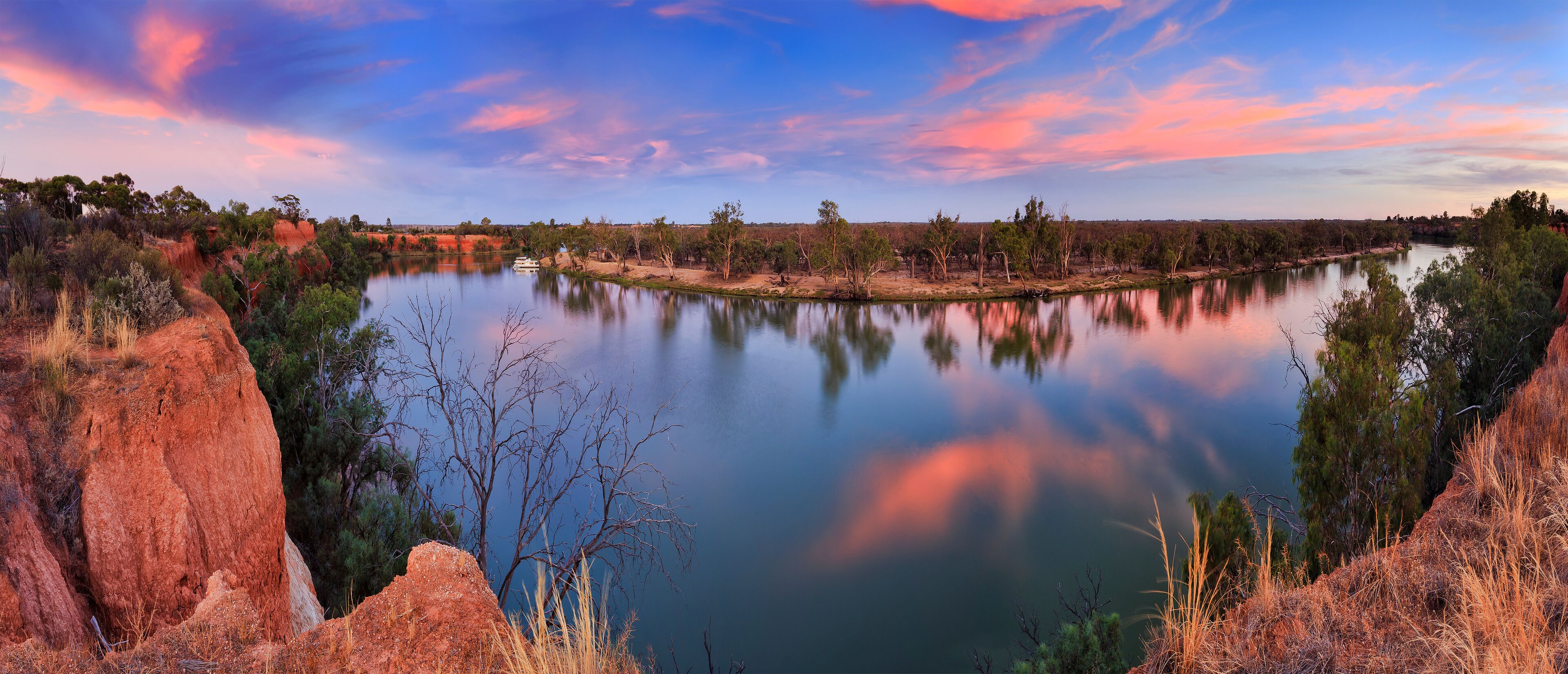A river with red cliffs and trees reflecting in the water.