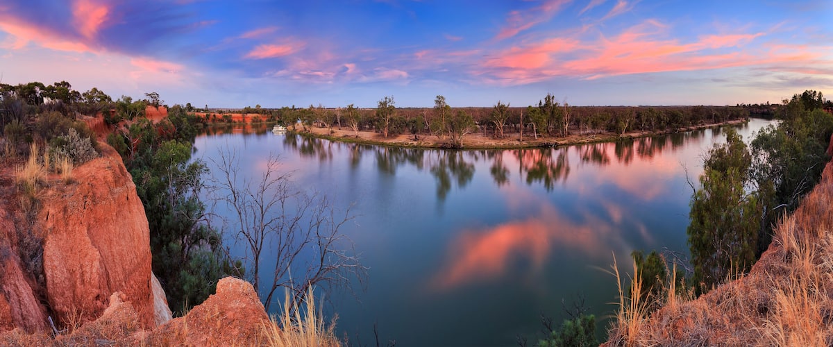 A river with red cliffs and trees reflecting in the water.