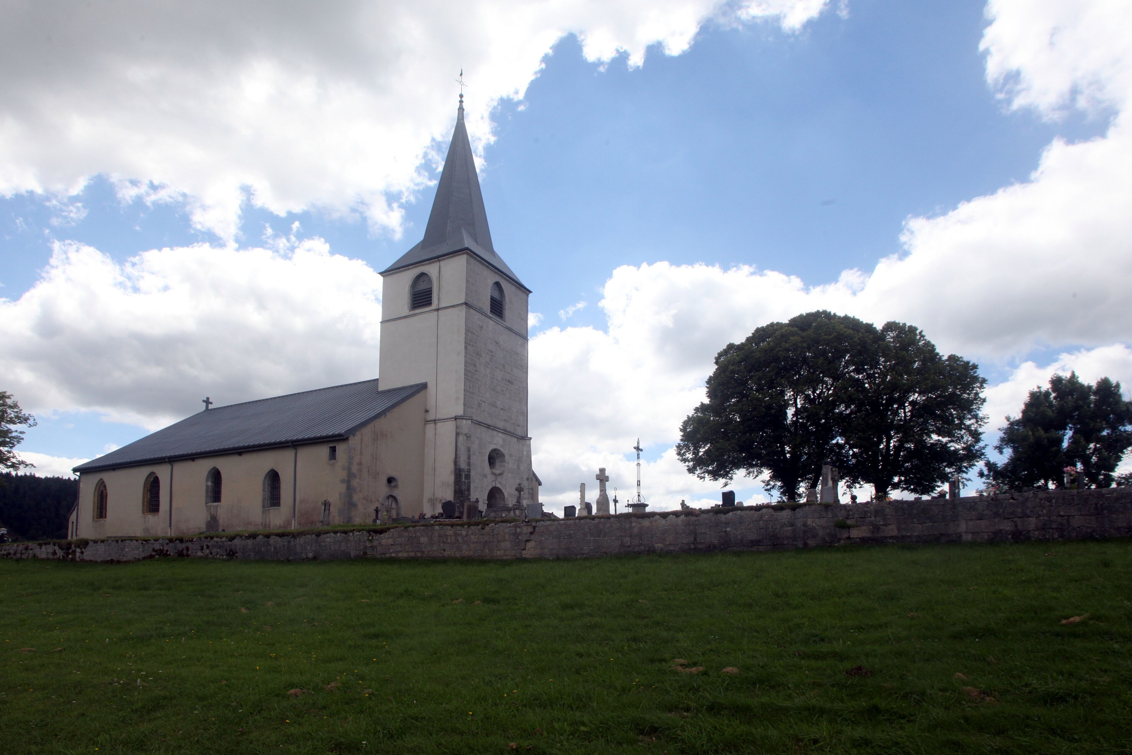 A church with a tall steeple and a stone wall in front.